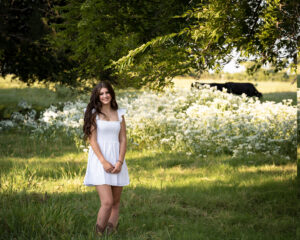 Girl standing in a wildflower field with cows in the background