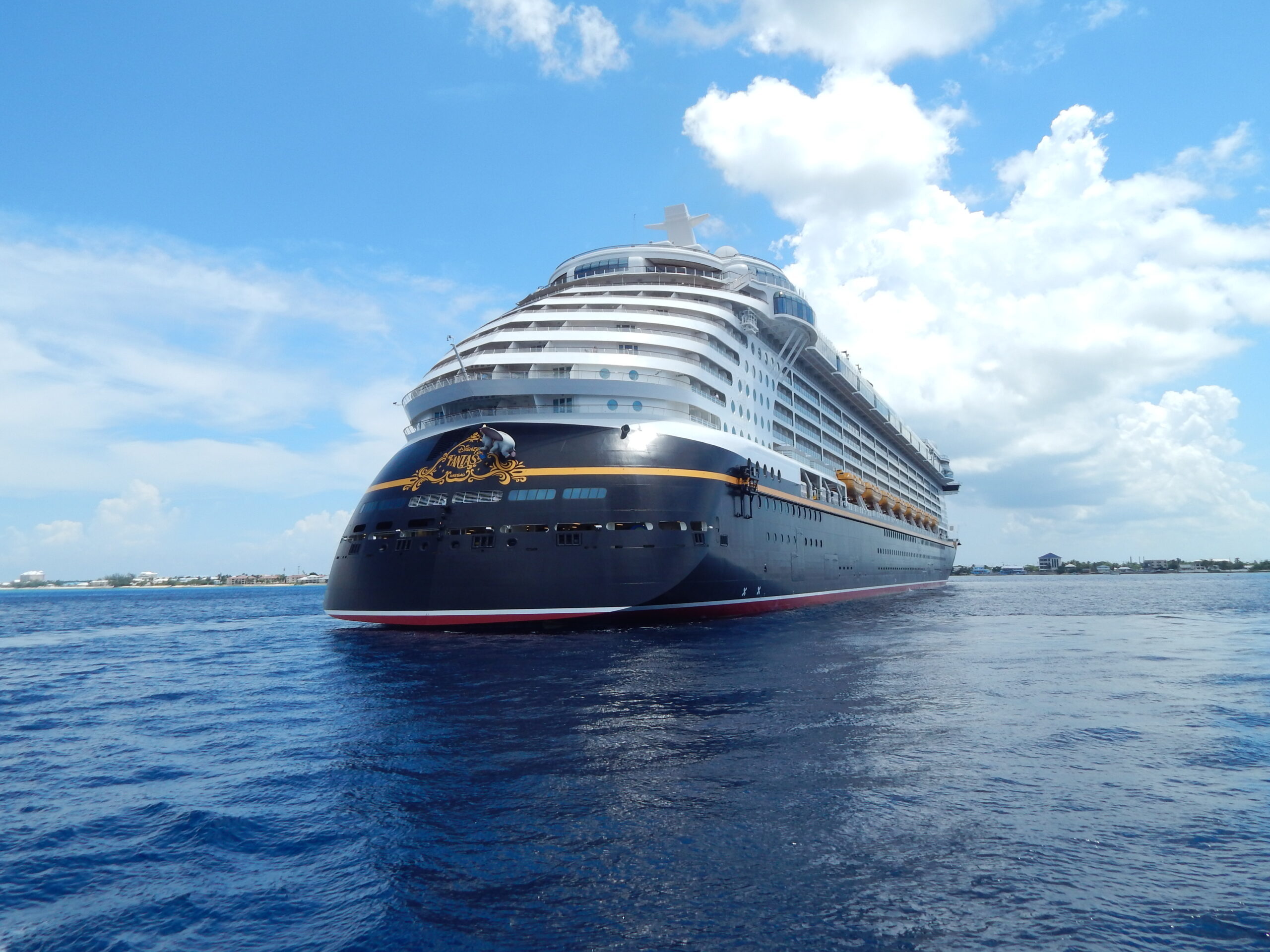 Disney cruise ship sitting in water with a beautiful blue sky and clouds
